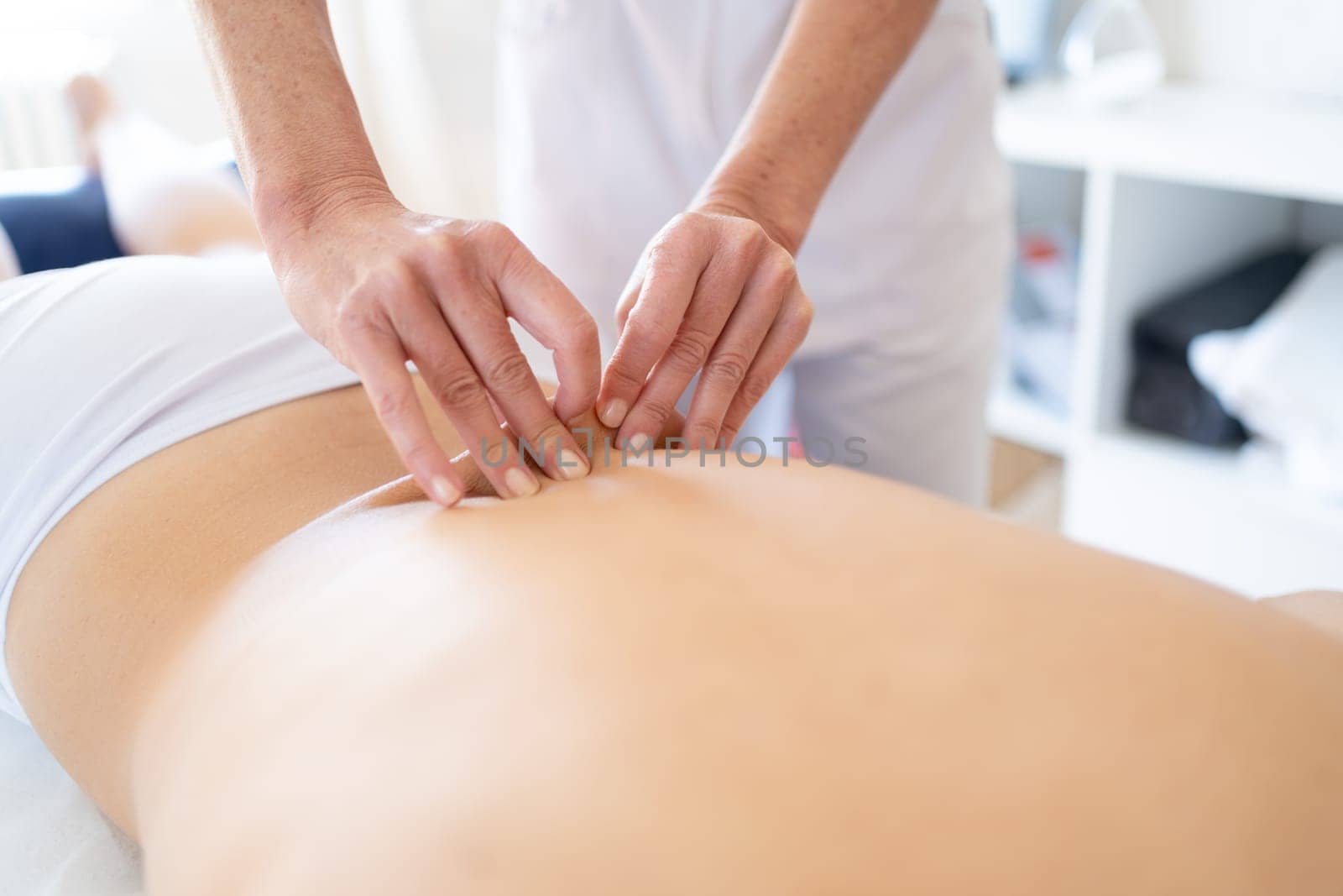 Crop anonymous female massage therapist rubbing back of patient with hands during rehabilitation session in manual therapy clinic