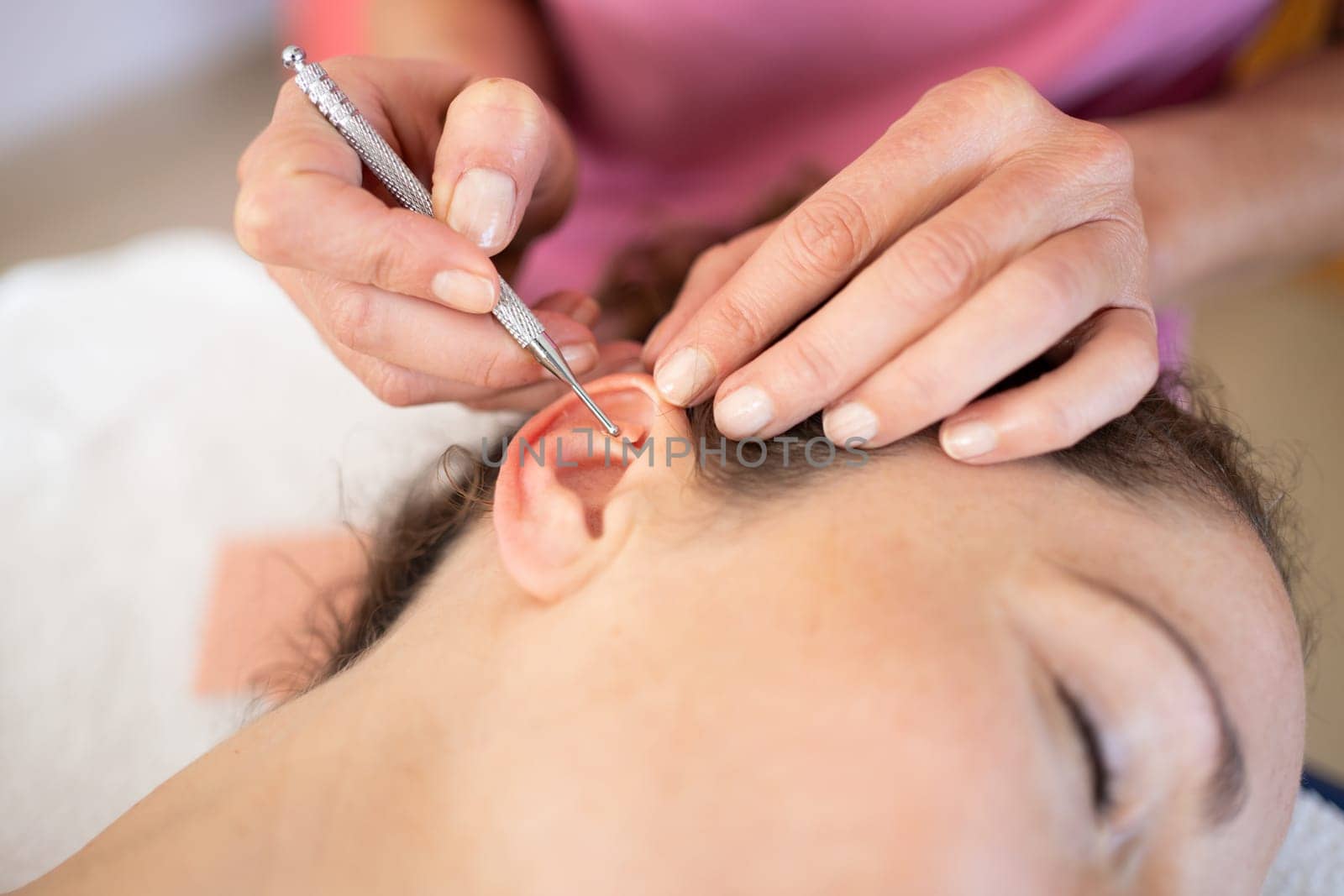 Crop chiropractor massaging ear of woman during auriculotherapy in beauty salon by javiindy