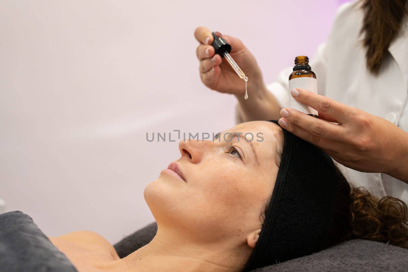 Crop beautician putting serum on client face in beauty salon by javiindy