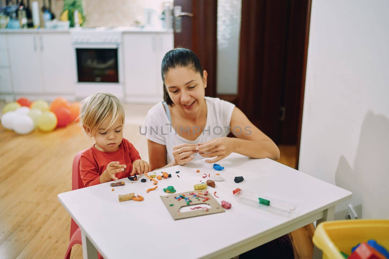 Mom with a little daughter make crafts from plasticine at the table. High quality photo