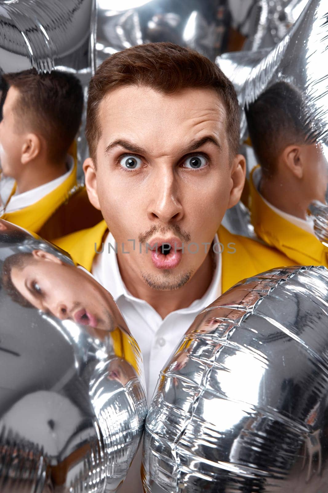 portrait of surprised man in yellow jacket with a lot of silver air balloons. birthday party