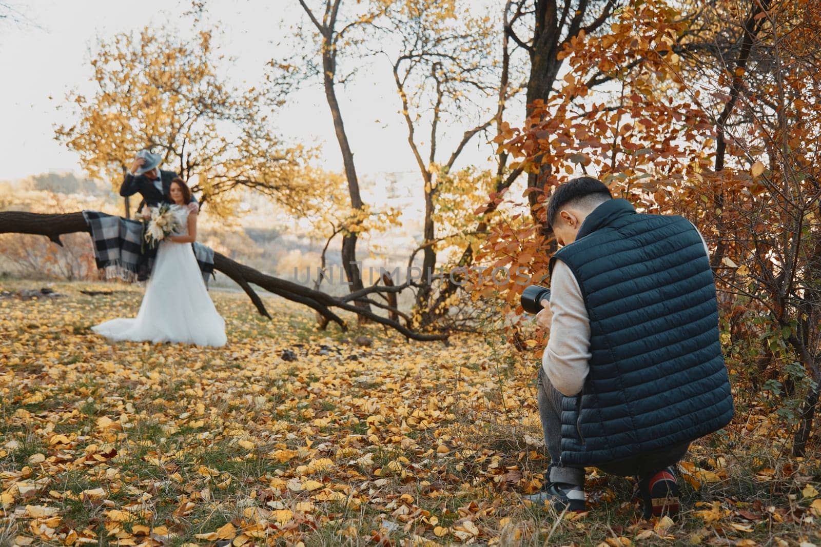 male wedding photographer taking pictures of the bride and groom outdoor in autumn