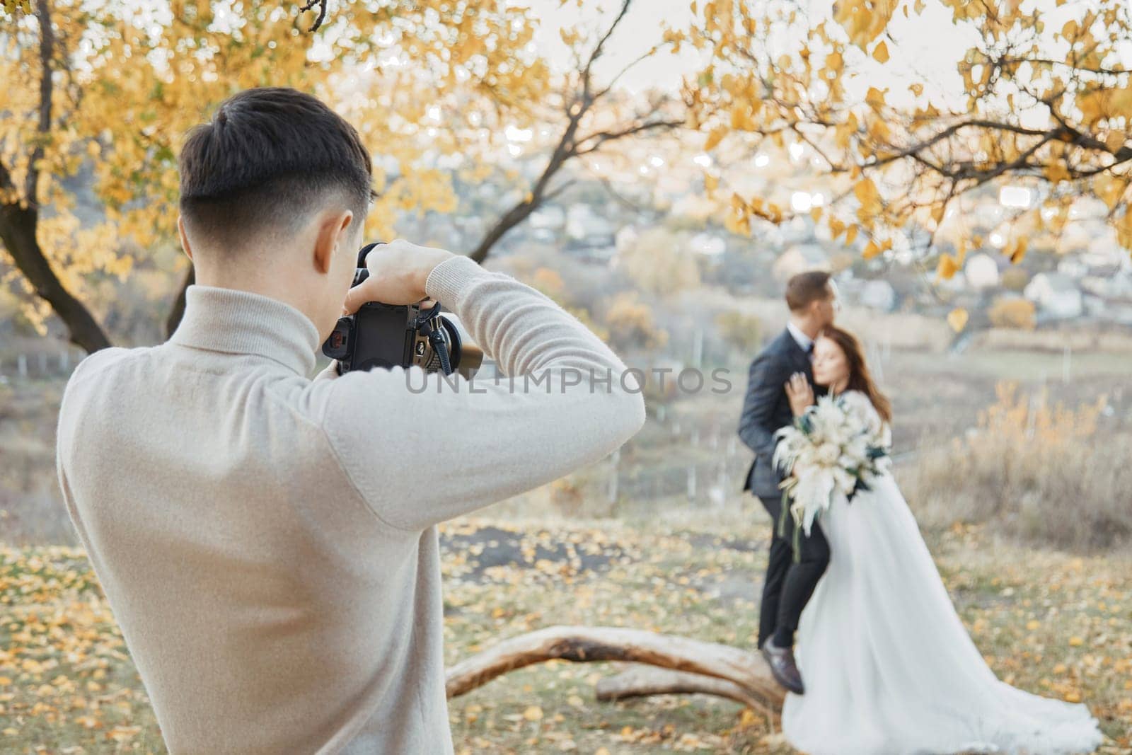 Professional wedding photographer taking pictures of the bride and groom in nature in autumn