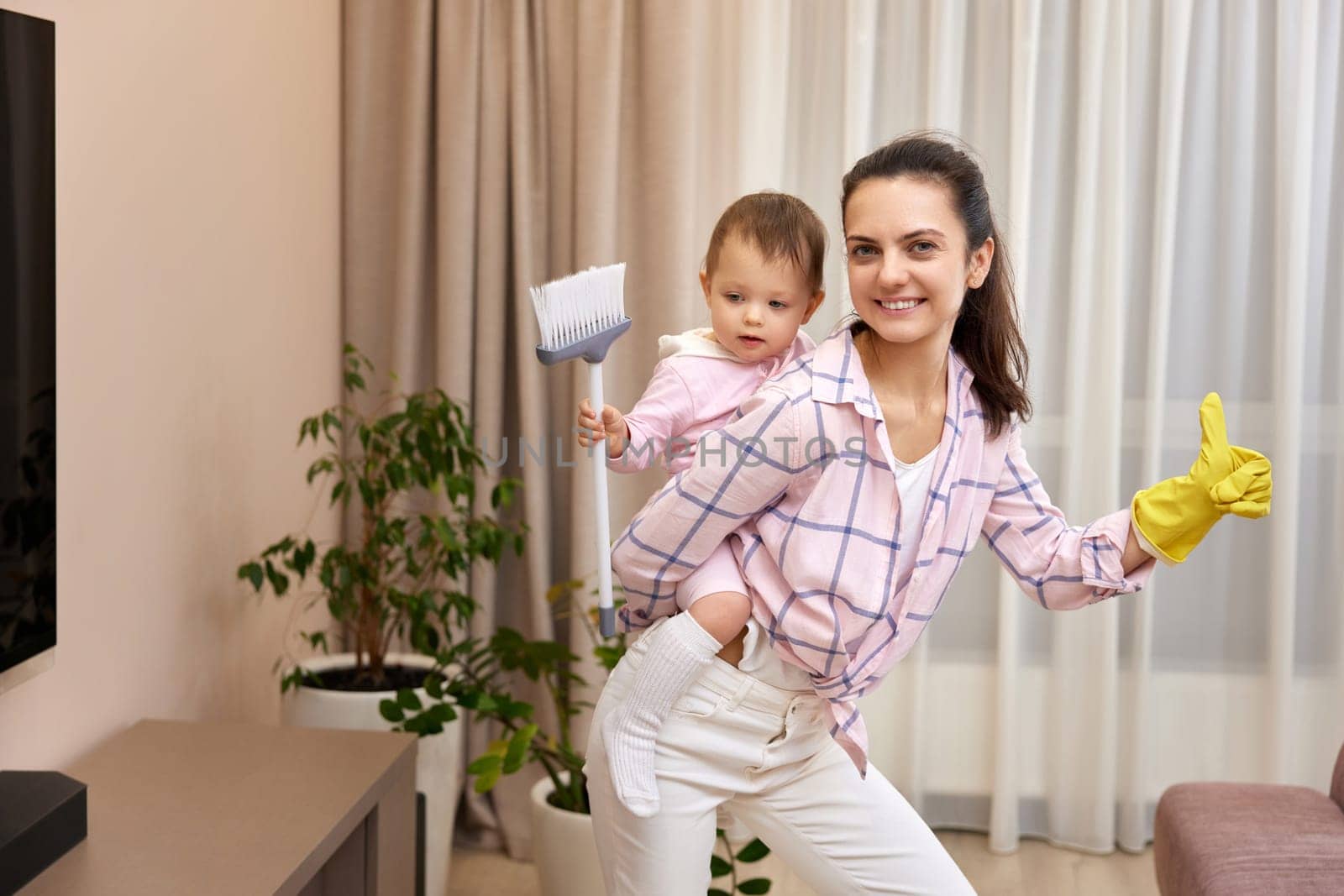 happy mother housewife is holding cute baby girl and doing housework at home, Happy family having fun