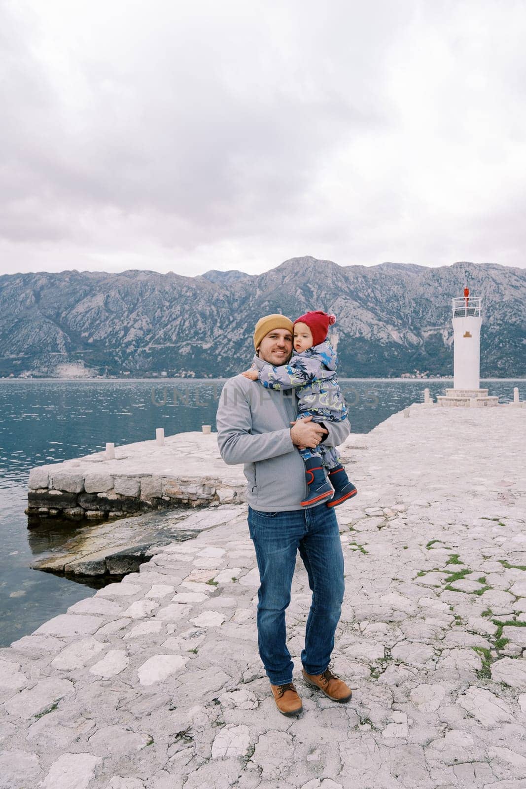 Dad with a little girl in his arms stands on the pier overlooking the lighthouse. High quality photo