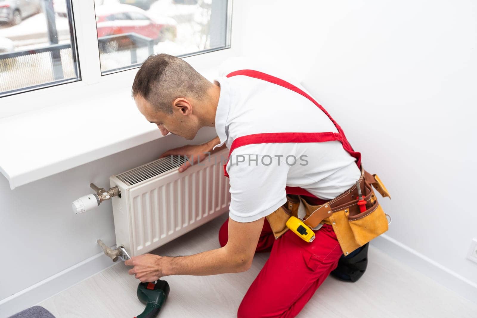 A male plumber installs a radiator in the heating system of an apartment. Guy in overalls and a gas wrench. High quality photo