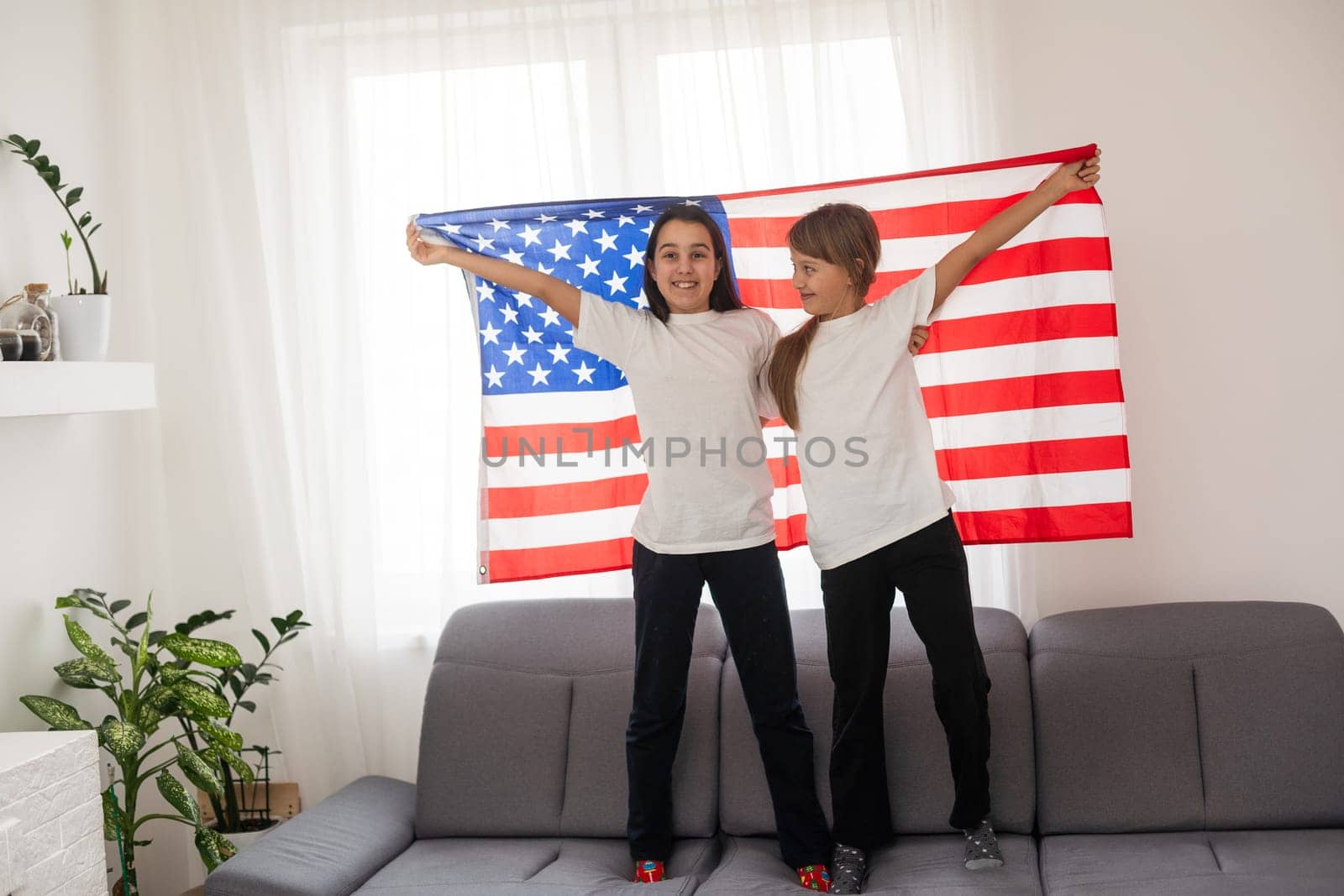 Brunette and blonde teenage girlfriends in white t-shirts holding american flag, energetic teenage friends spending time, friendship by Andelov13