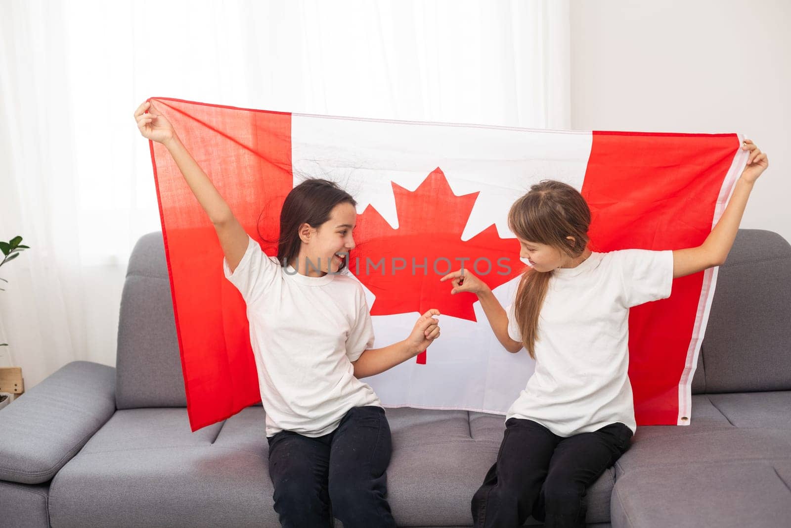 Happy Canada Day Celebration. Two girls with braided hair are at nature background with big Canada flag in their hands. Young Canadian caucasian kids 1st of July. High quality photo