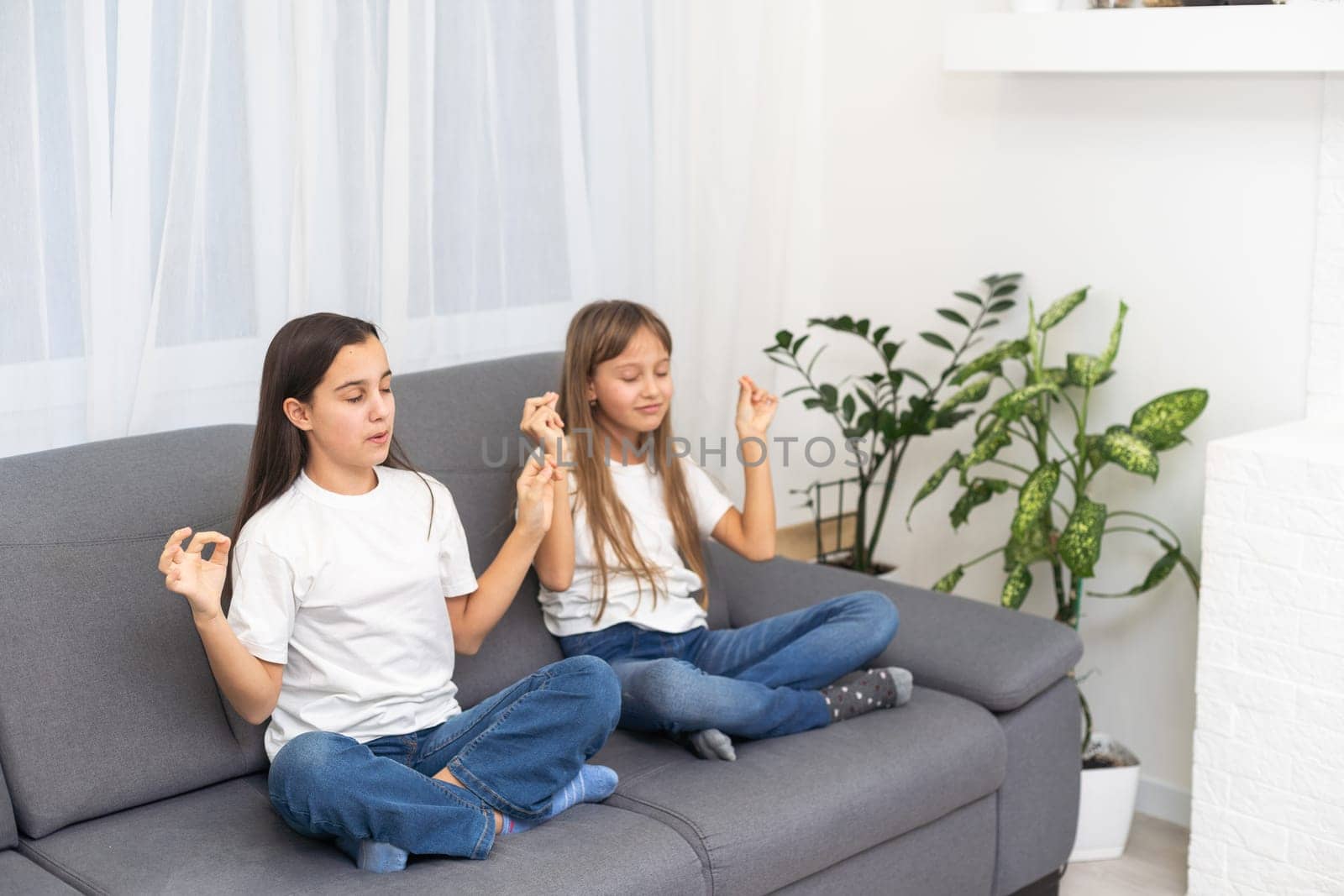 People, relationships, family, relaxation, yoga and meditation concept. girls sitting on bed, looking up, making mudra gesture, praying or meditating by Andelov13