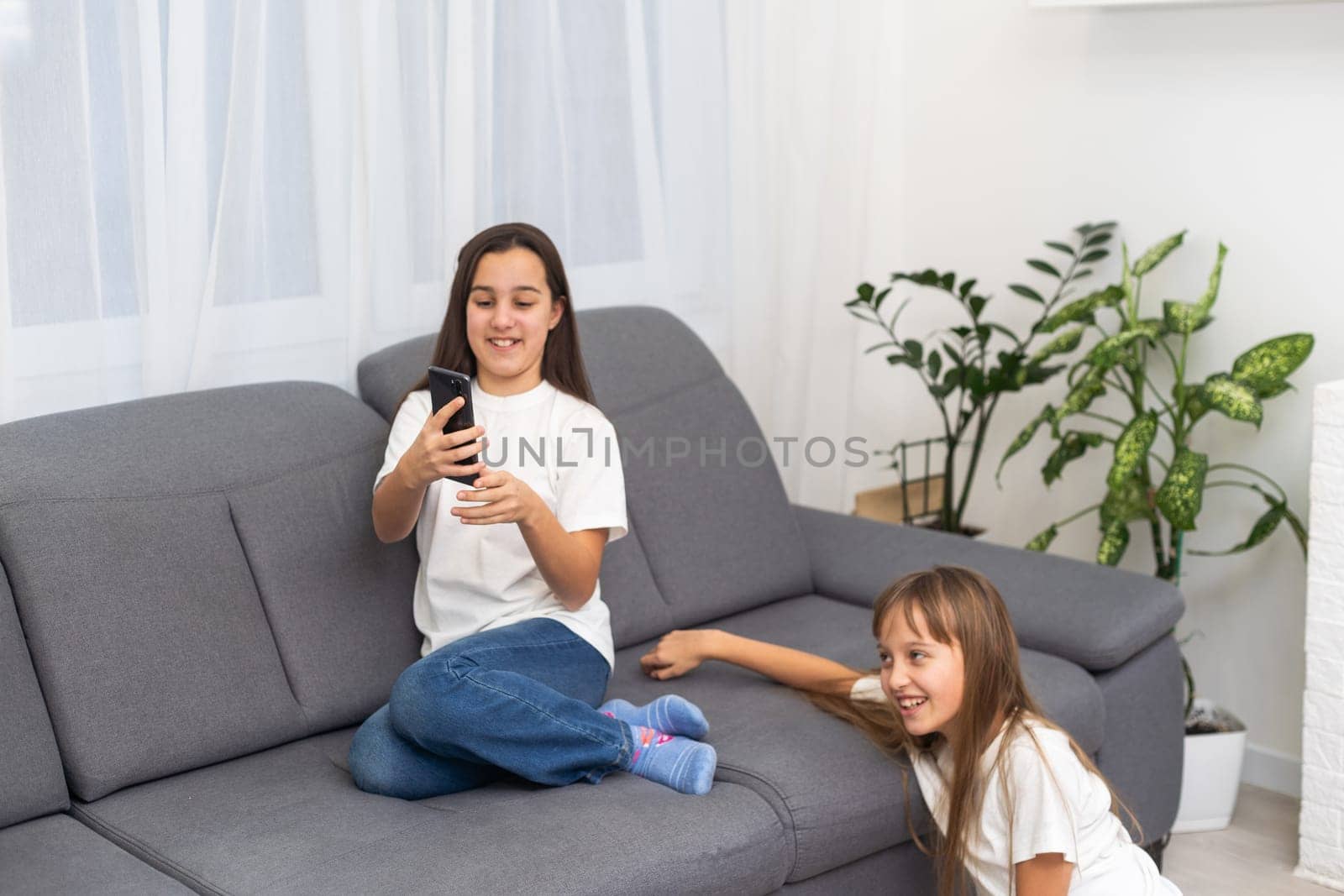 Two cute Caucasian blonde girls sisters holding cell phone and laughing. High quality photo