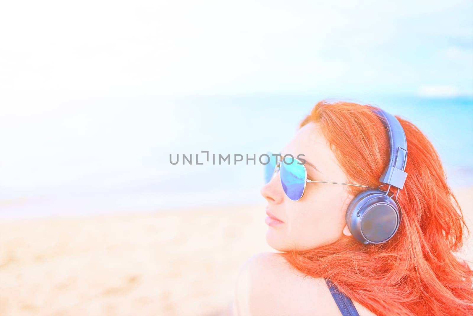 Elegant woman listening to music on the beach. Young female listening to music with headphones.
