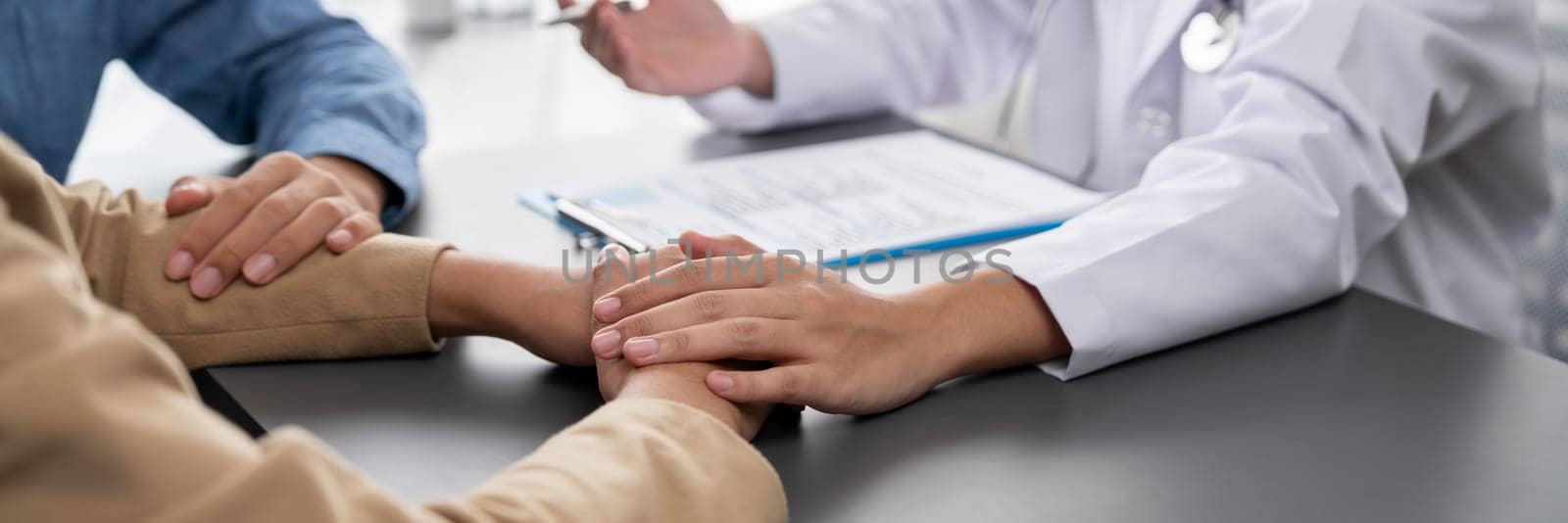 Doctor providing compassionate healthcare consultation while young couple patient holding hand, comfort each other after infertile report. Reproductive and medical fertility consulting. Neoteric