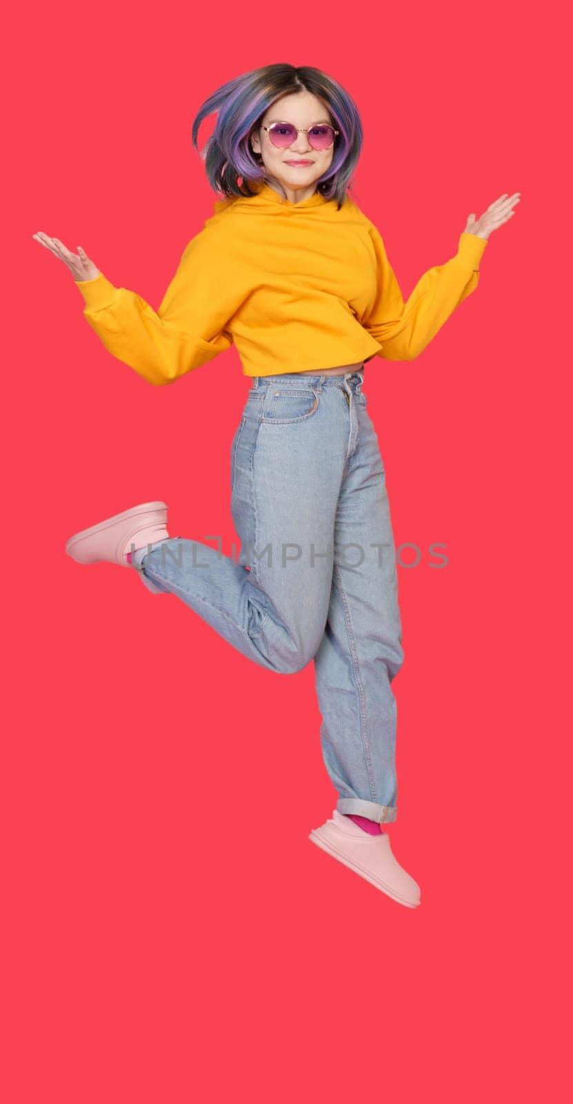 Smiling Asian girl teenager in mid-jump against vibrant red color background. Exuberance and happiness of youth, showcasing dynamic and lively nature of teenager in moment of pure joy and positivity. by LipikStockMedia
