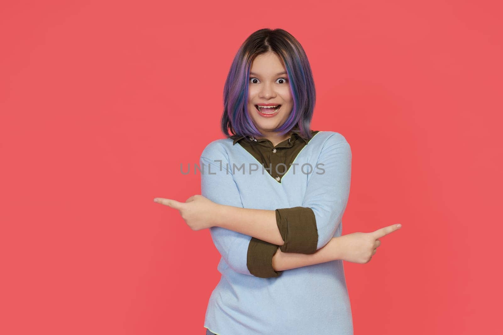 Happy teenager girl points in two opposite directions, creating copy space with hands, offering inviting opportunity to make choice or buy services. by LipikStockMedia