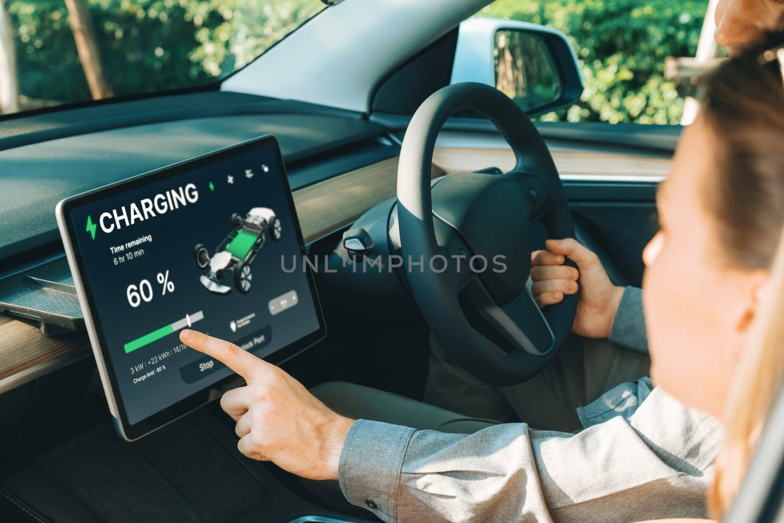 Electric car driver checks battery charging status, range and charging limit on app screen in the car. Smart technology device show EV car recharging data of electric storage in car battery innards.