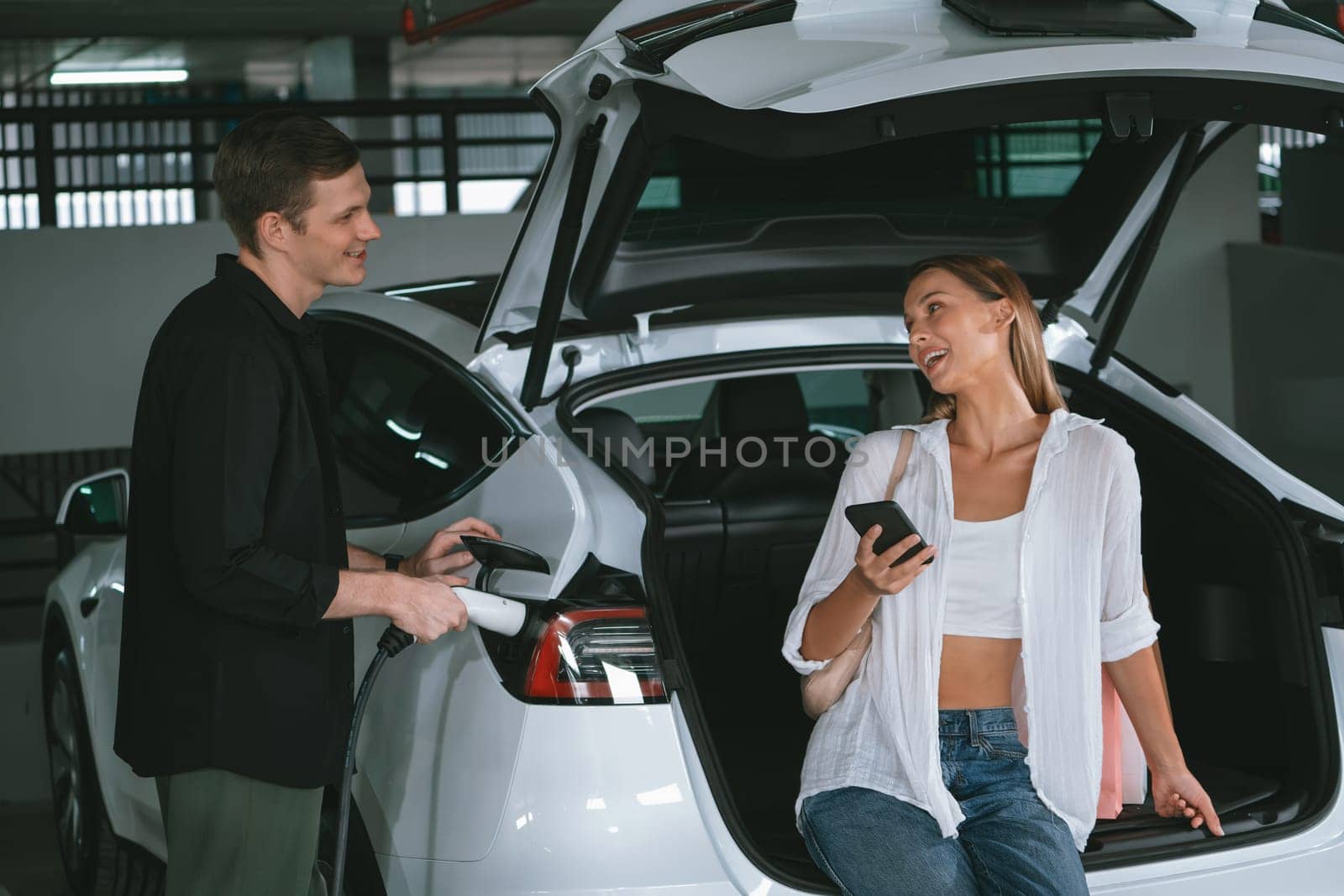 Young couple travel with EV electric car to shopping center parking lot innards by biancoblue
