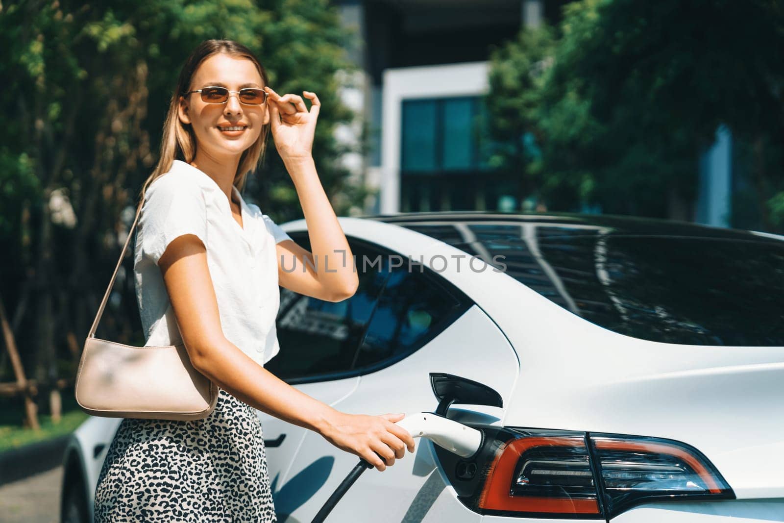 Young woman travel with EV electric car in green sustainable city innards by biancoblue