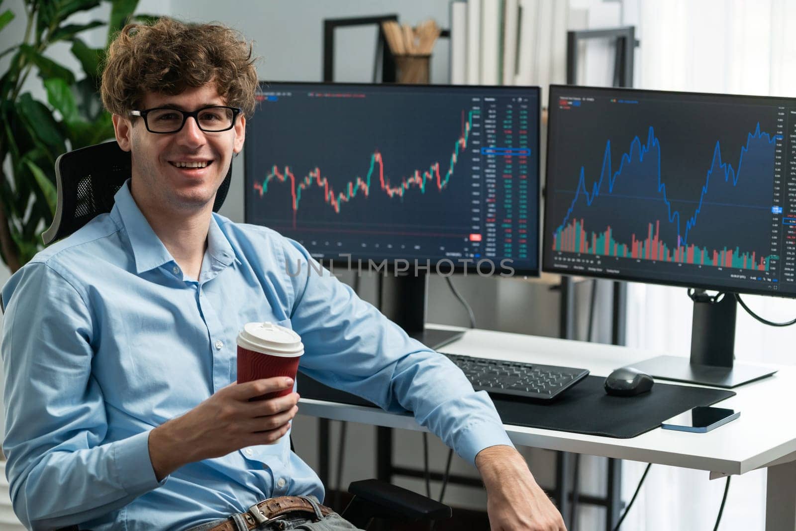 Profile of young stock trader with curly hair sitting against on dynamic financial exchange trading data screen while holding coffee up. Concept of professional business digital investment. Gusher.