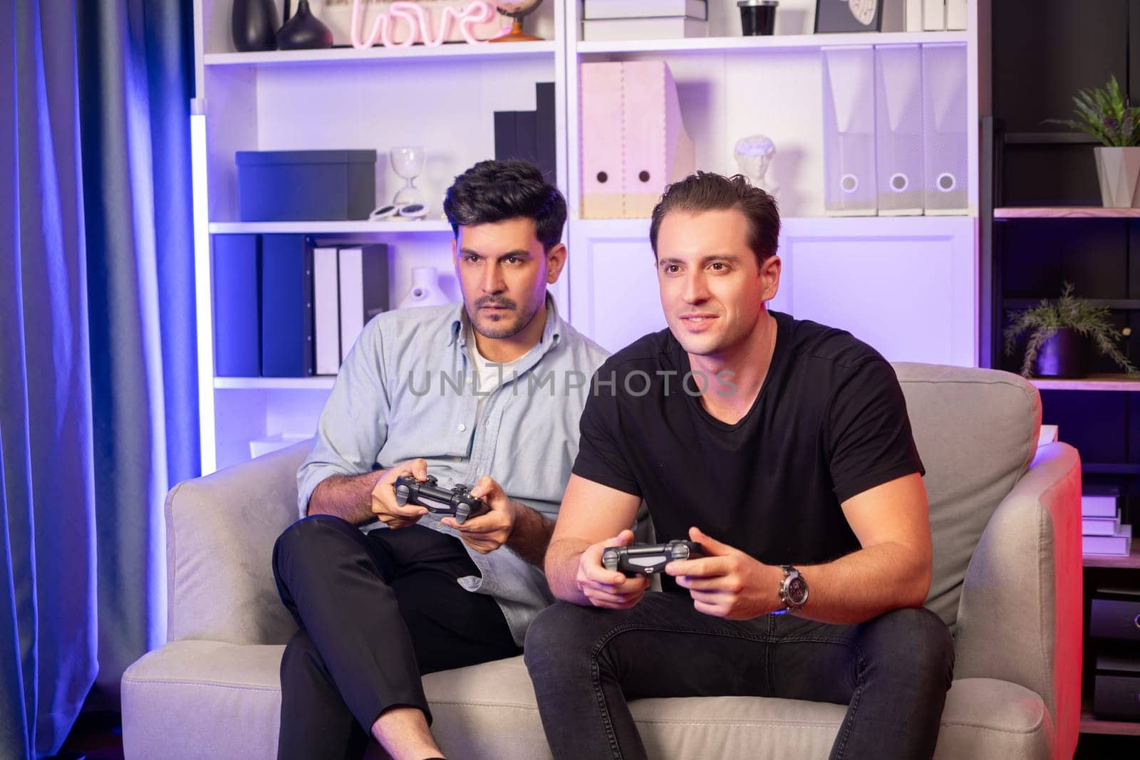 Winner and loser players of buddy friend gamers playing video game on TV using joysticks in studio room with neon blue light. Comfy living indoor at home place with cheerful fighting winner. Sellable.