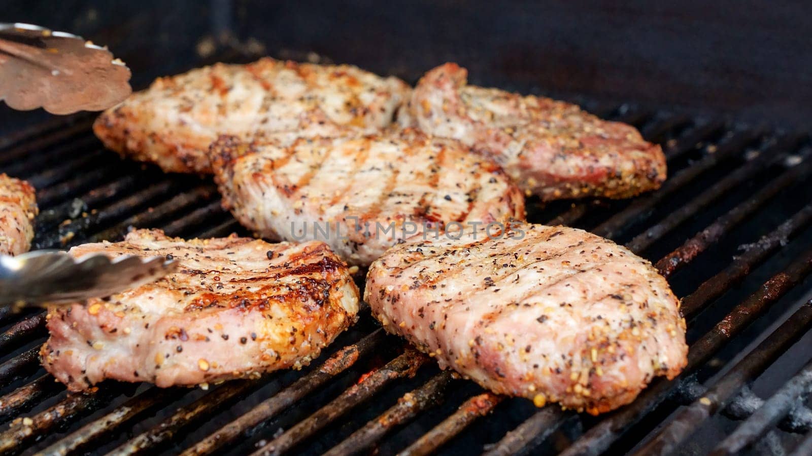 Grilled meat steak on stainless BBQ grill with flames on dark background. Food and cuisine concept