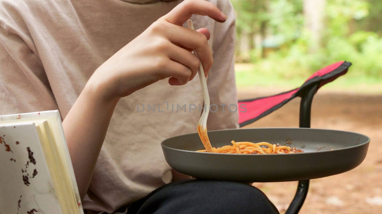 Unrecognizable young woman having summer picnic eating spaghetti outside in forest camping. Summer outdoors activities. Backyard picnic