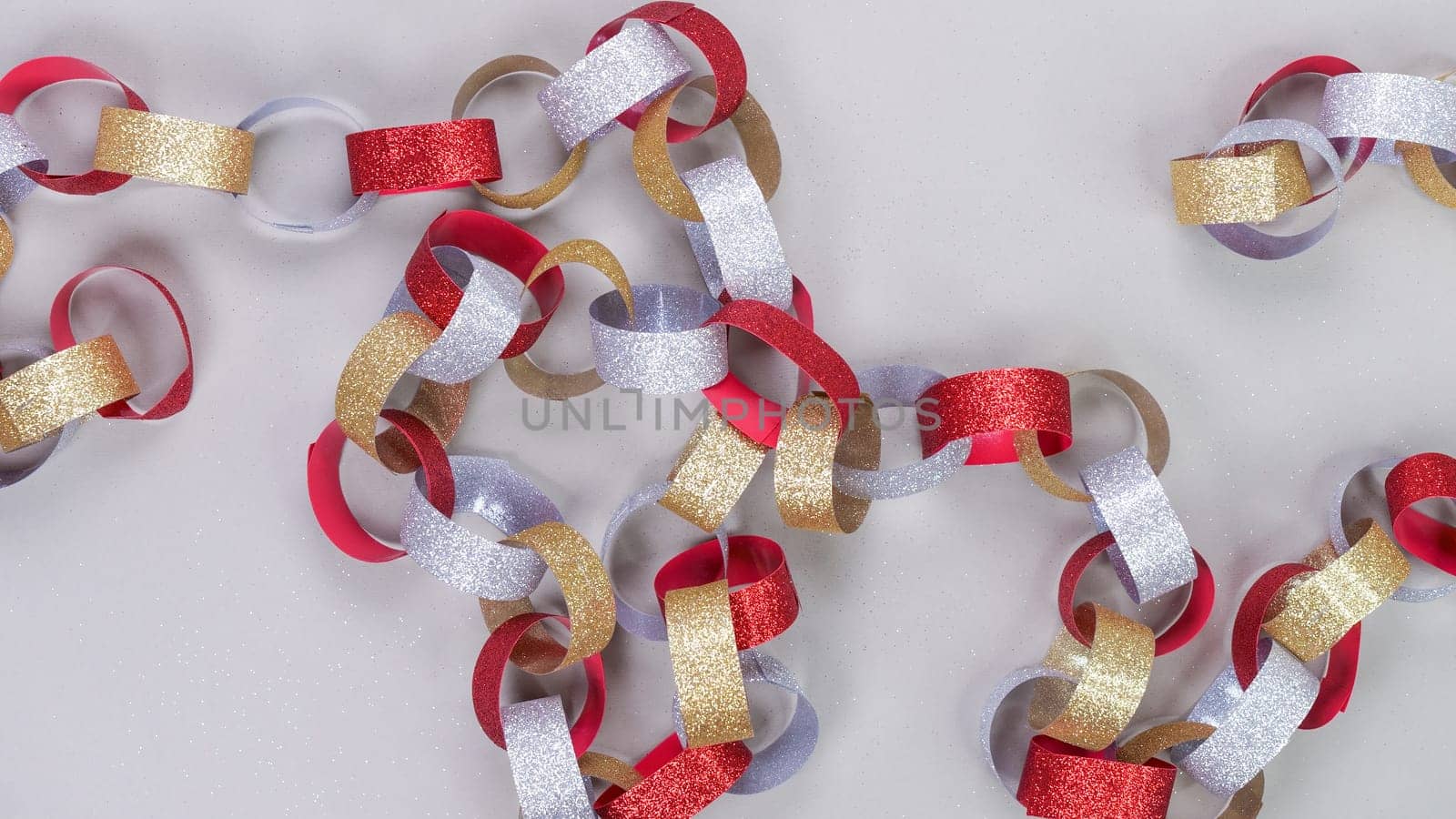 Colorful background with strips of gold silver red sparkling chain garland on grey. Festive Christmas birthday decoration garland.Space for text. by JuliaDorian