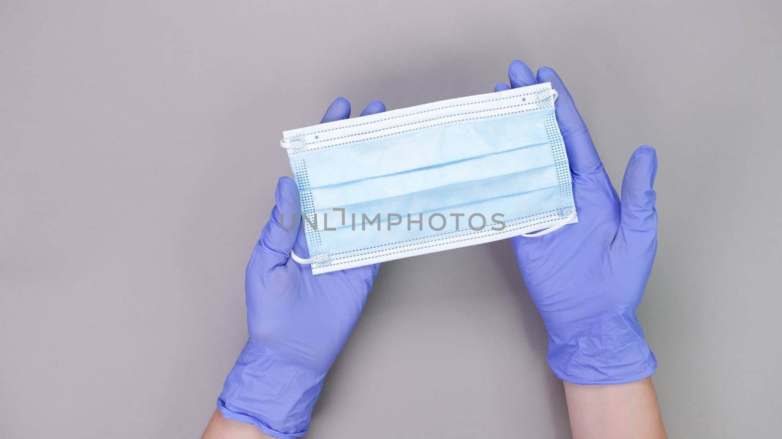 Hand in blue gloves of doctor or nurse holding protective blue face mask over grey background with copy space. New vaccine. Unknown vaccine. Medical gloves