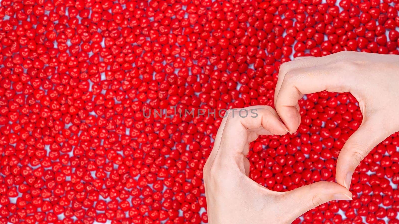 Woman hands making heart shape on red candy background. Heart from hands. Valentines Day concept. Symbol and shape of heart created from hands. Red peppermint candy. The concept of unity and charity