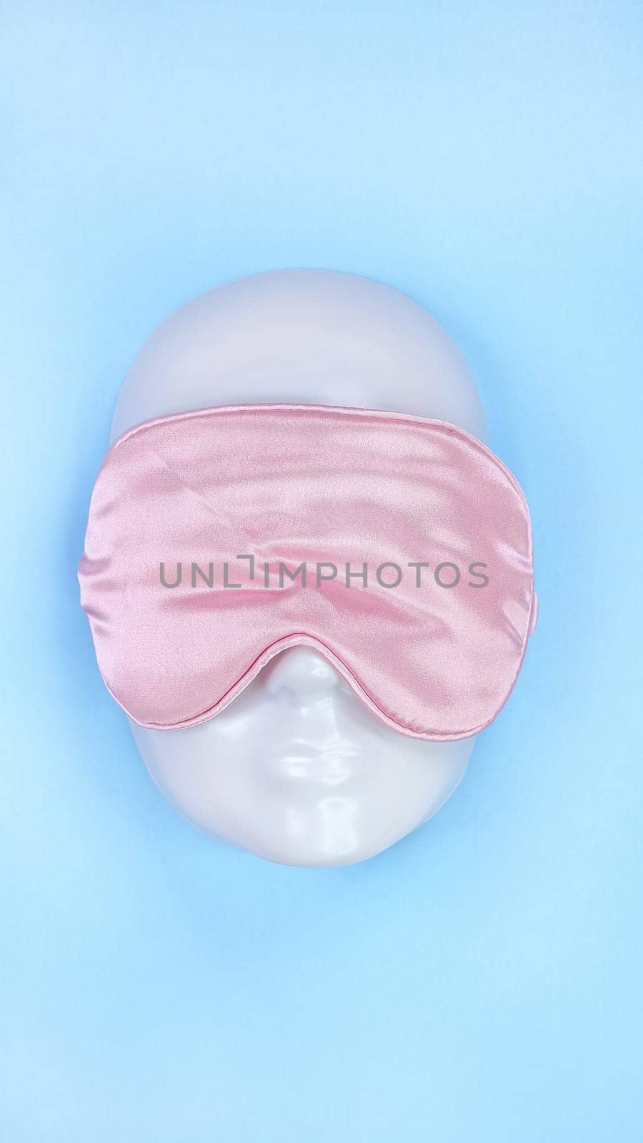 Pink sleeping eye mask on white mannequin face on blue background, sleeping disorder. Valentine day. Holidays, Head accessory. Plastic face