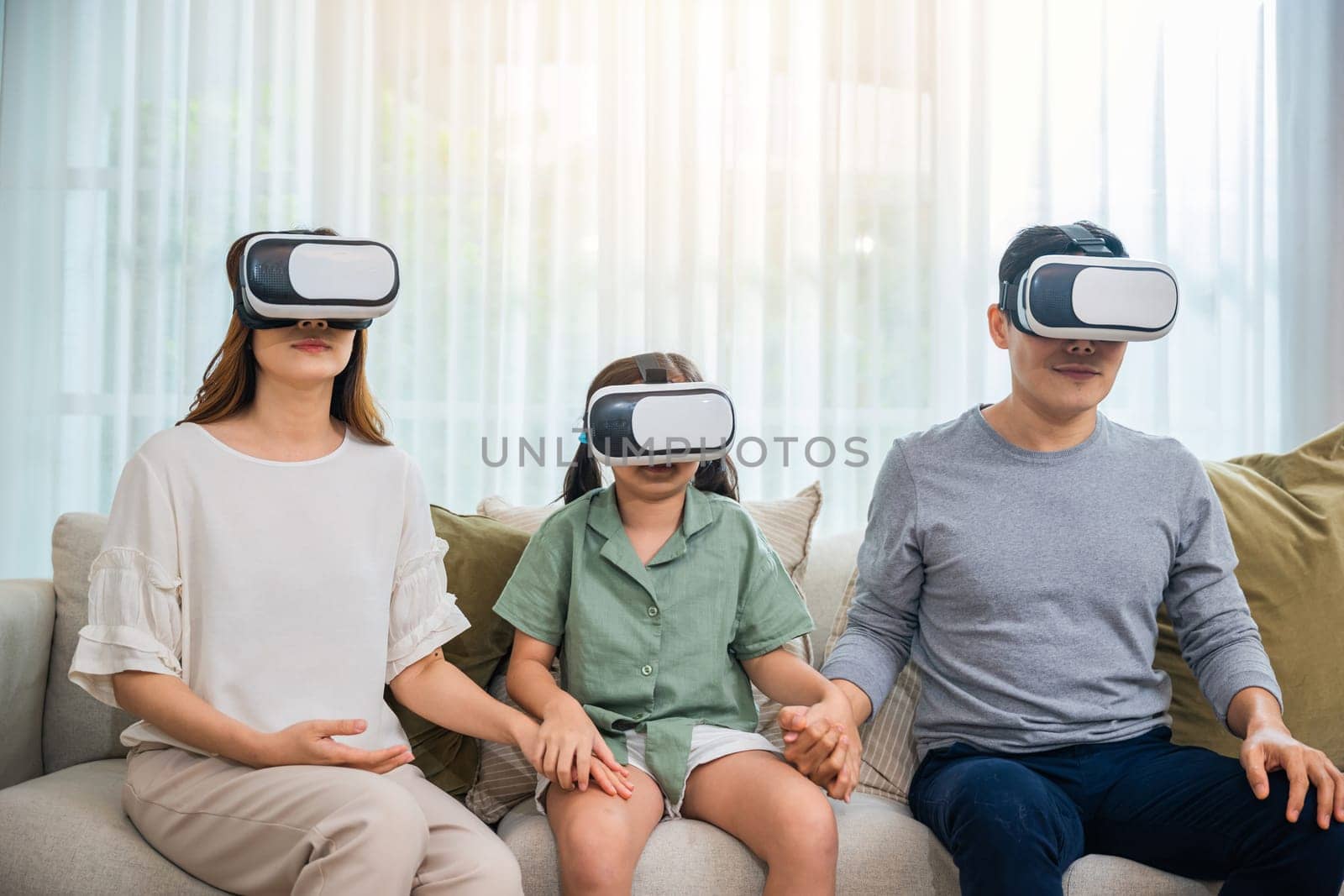 Asian family wear vr glasses headsets sitting on sofa in living room, game entertainment innovation technology, Happy family have mother father and daughter watching movie or playing video game