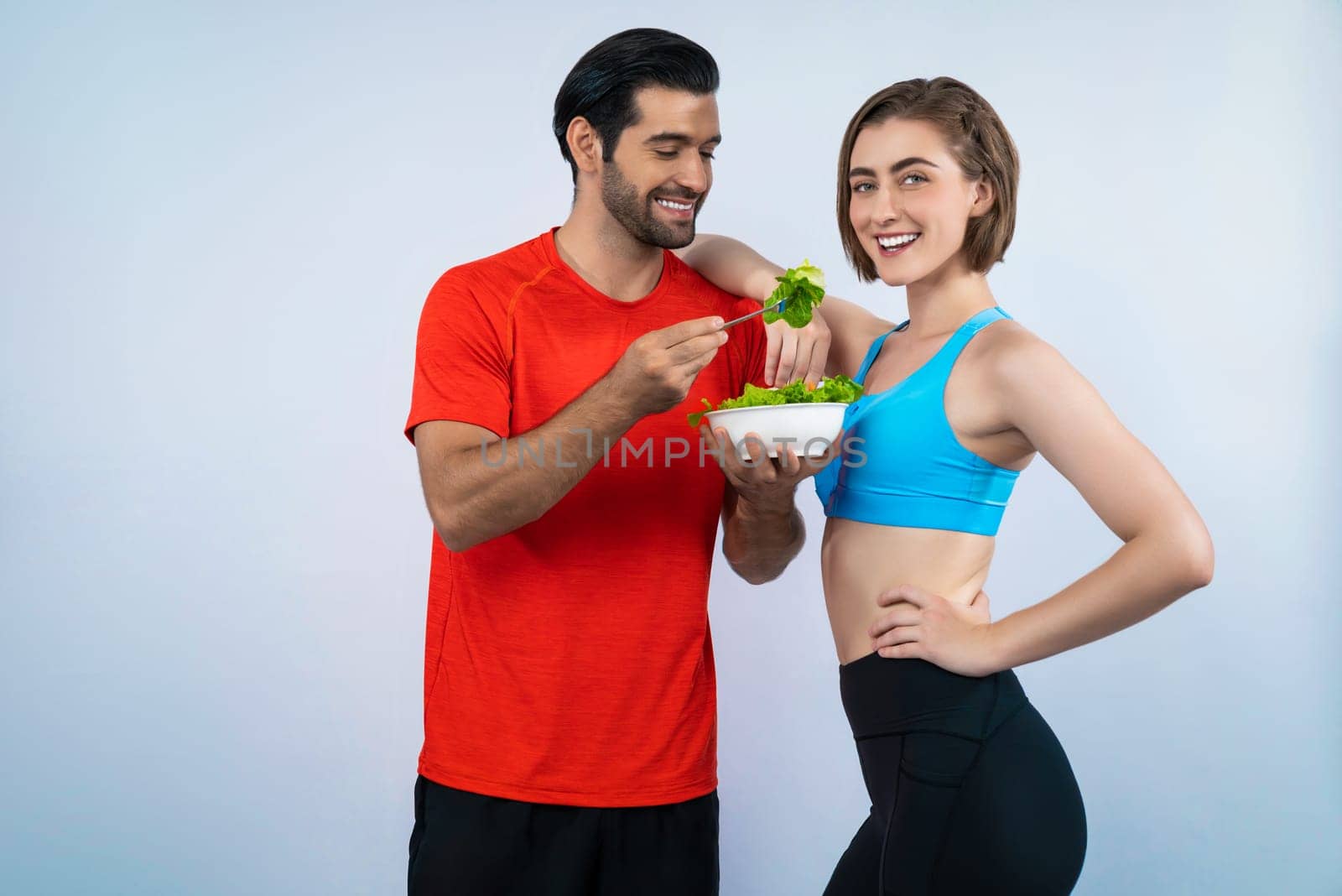 Full body length gaiety shot athletic and sporty young couple with healthy vegan food in standing posture on isolated background. Healthy active and body care by vegetarian lifestyle.