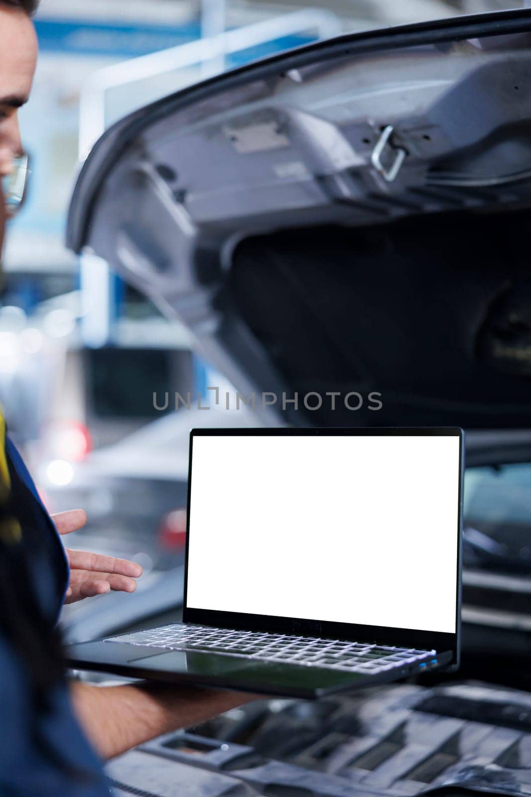 Experienced serviceman in garage using mockup laptop to follow checklist while doing maintenance on car. Hardworking professional in repair shop does checkup on vehicle with isolated screen device