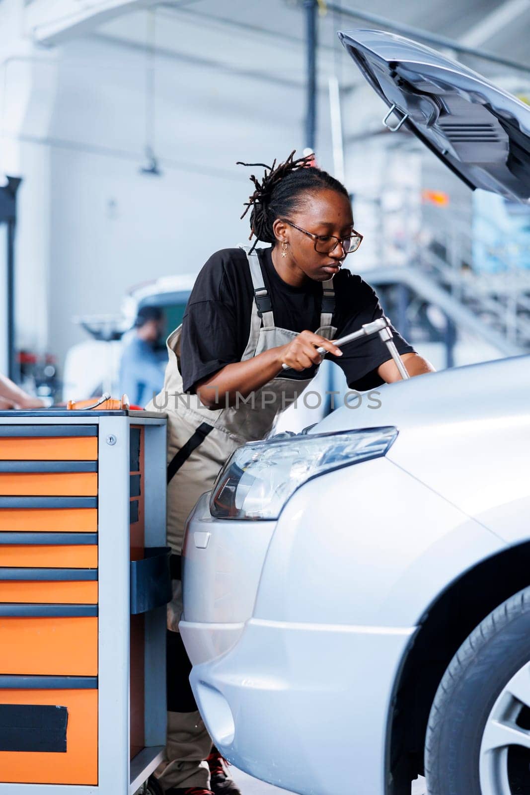 Engineer in car service use torque wrench to tighten bolts after replacing engine. African american skilled auto repair shop employee uses professional tools to fix customer automobile