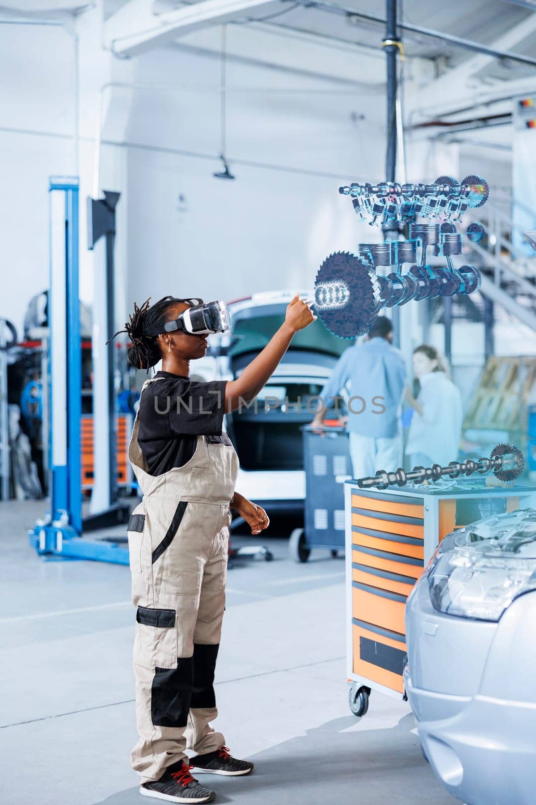 Qualified engineer in repair shop using VR googles and augmented reality hologram to visualize car parts in order to fix them. BIPOC woman using AR technology while working on damaged vehicle motor