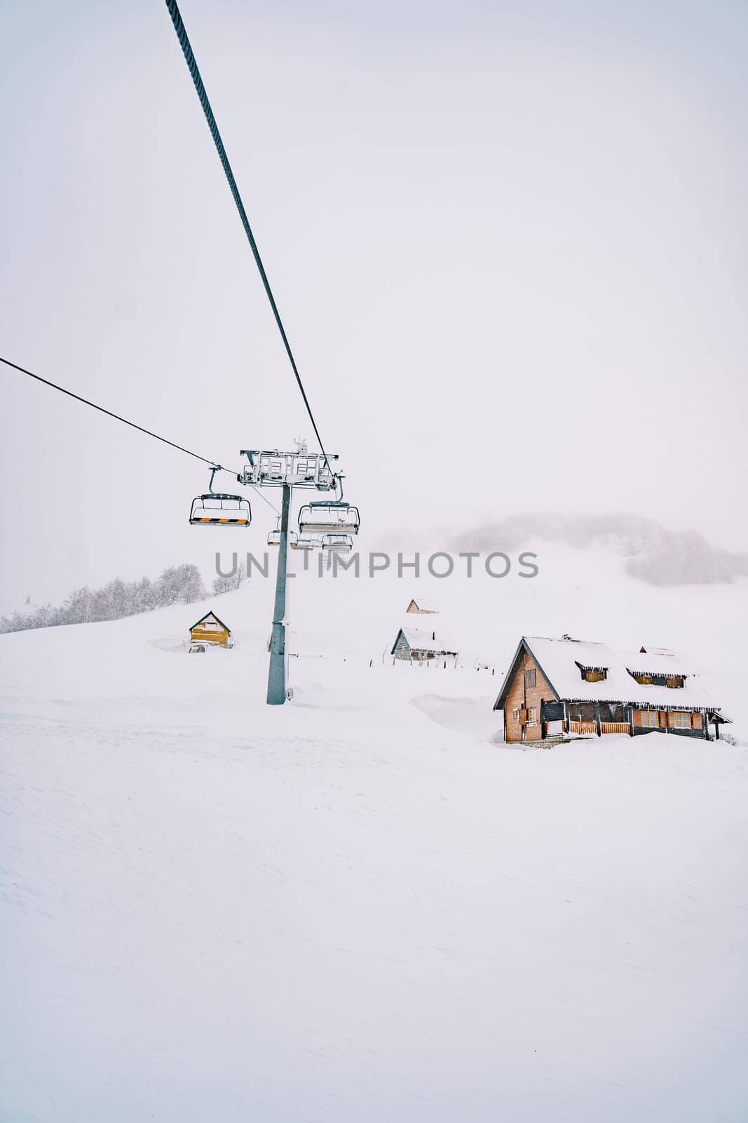 Chairlift passes by wooden cottages on a snow-capped mountain. High quality photo