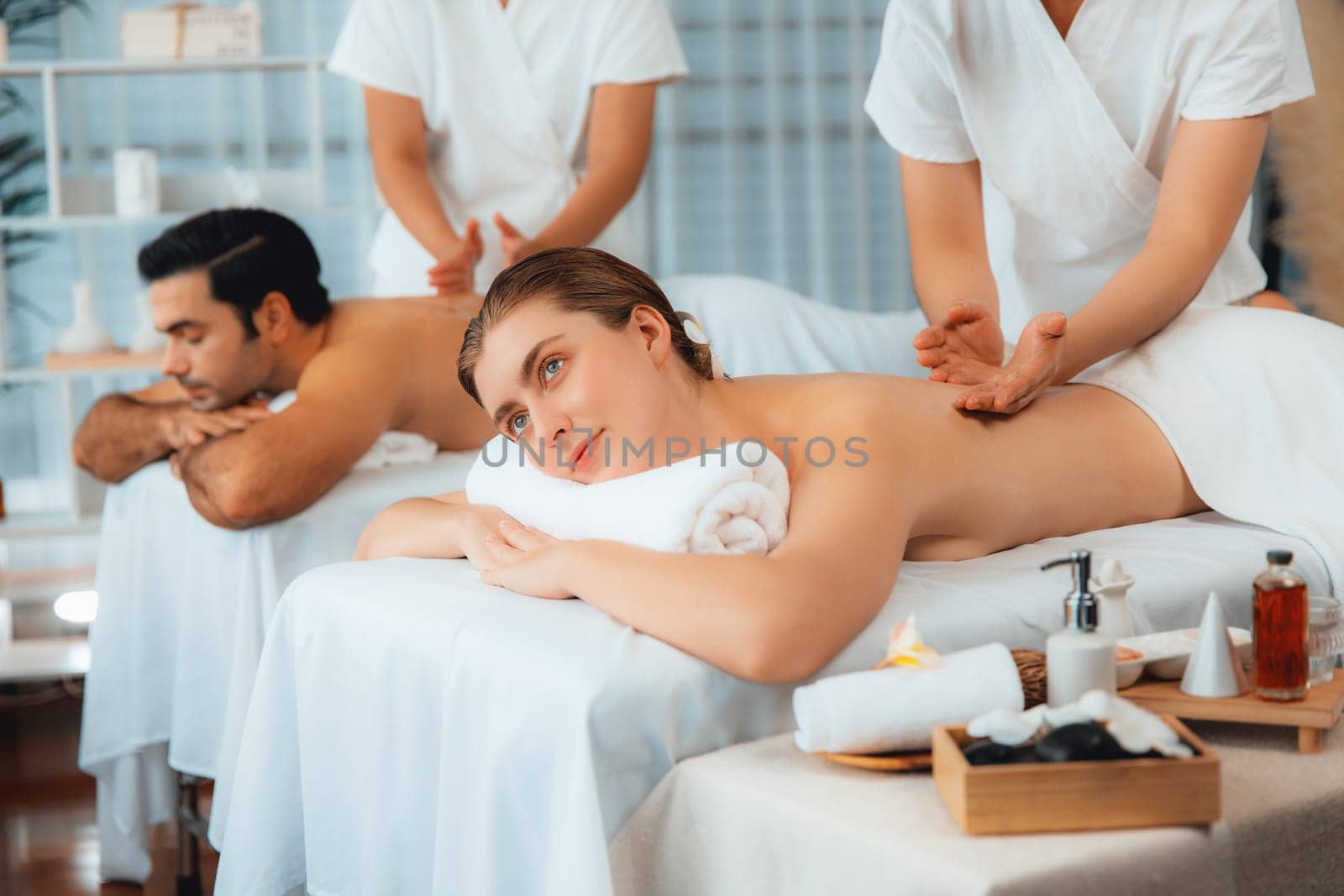 Caucasian couple customer enjoying relaxing anti-stress spa massage and pampering with beauty skin recreation leisure in day light ambient salon spa at luxury resort or hotel. Quiescent