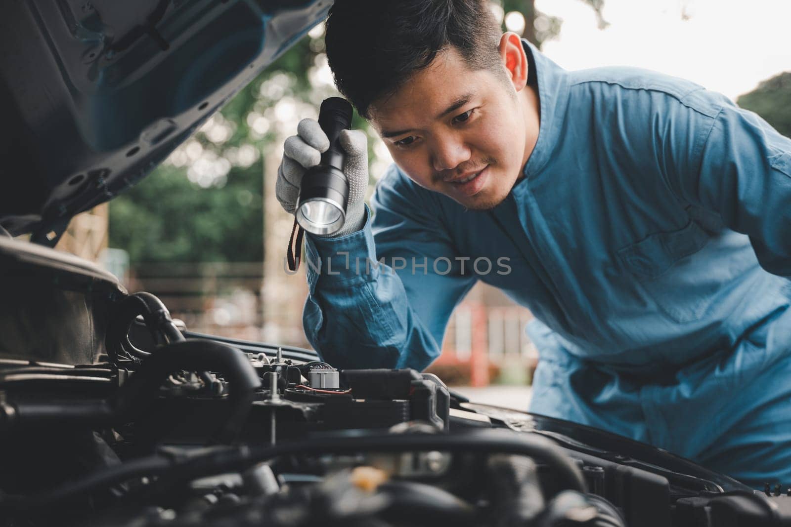 Young repairman analyzing car problems with an electric lamp on the road. Expert car mechanic repairer checking and repairing auto engine.