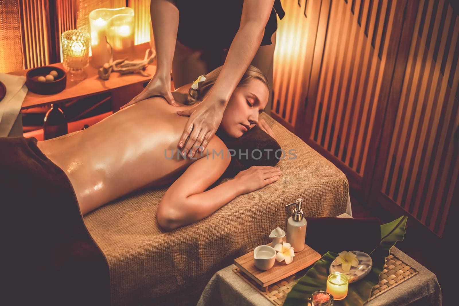 Caucasian woman customer enjoying relaxing anti-stress spa massage and pampering with beauty skin recreation leisure in warm candle lighting ambient salon spa at luxury resort or hotel. Quiescent