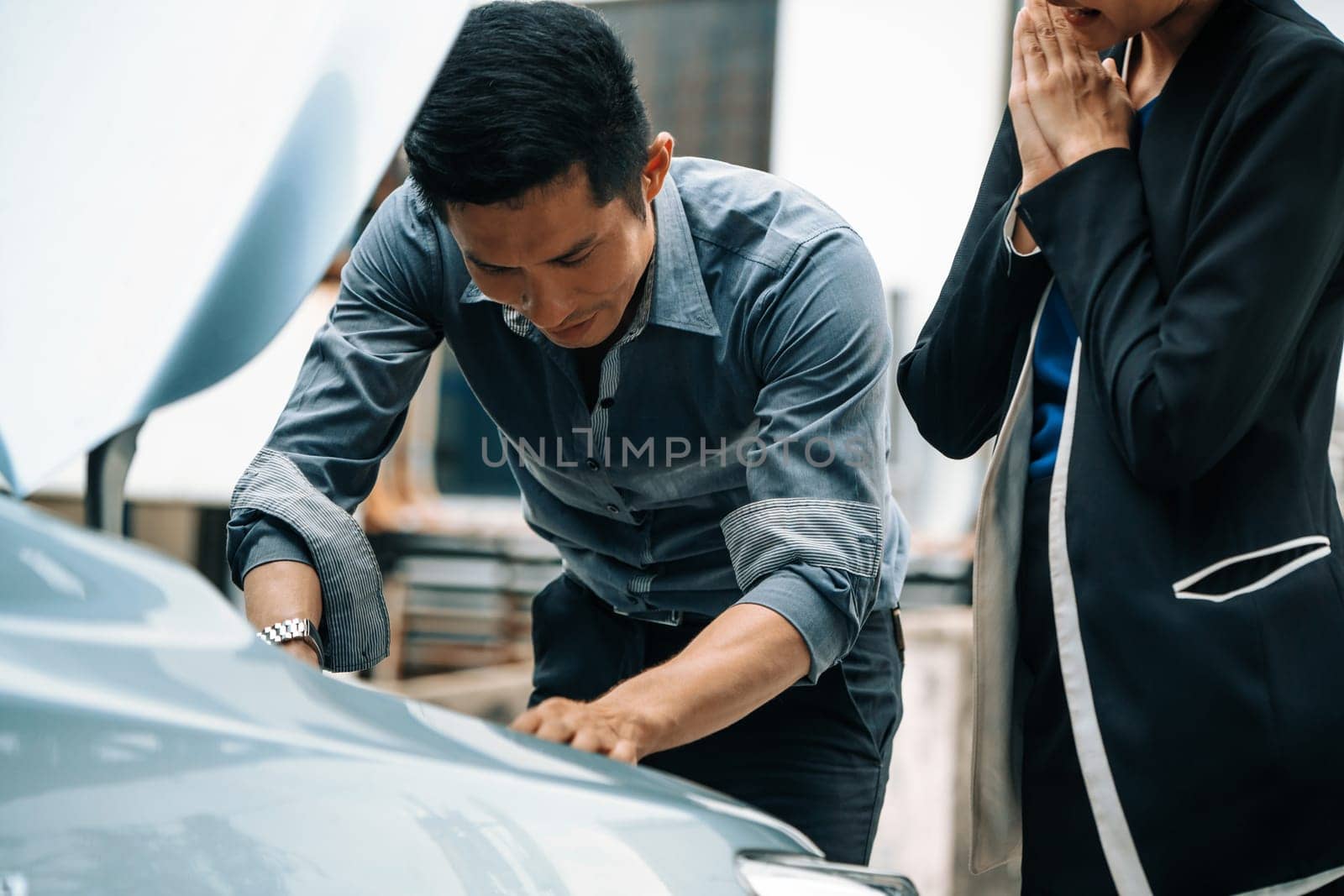 Man help woman fix the car problem. He pop up the car hood to repair the damaged part. uds