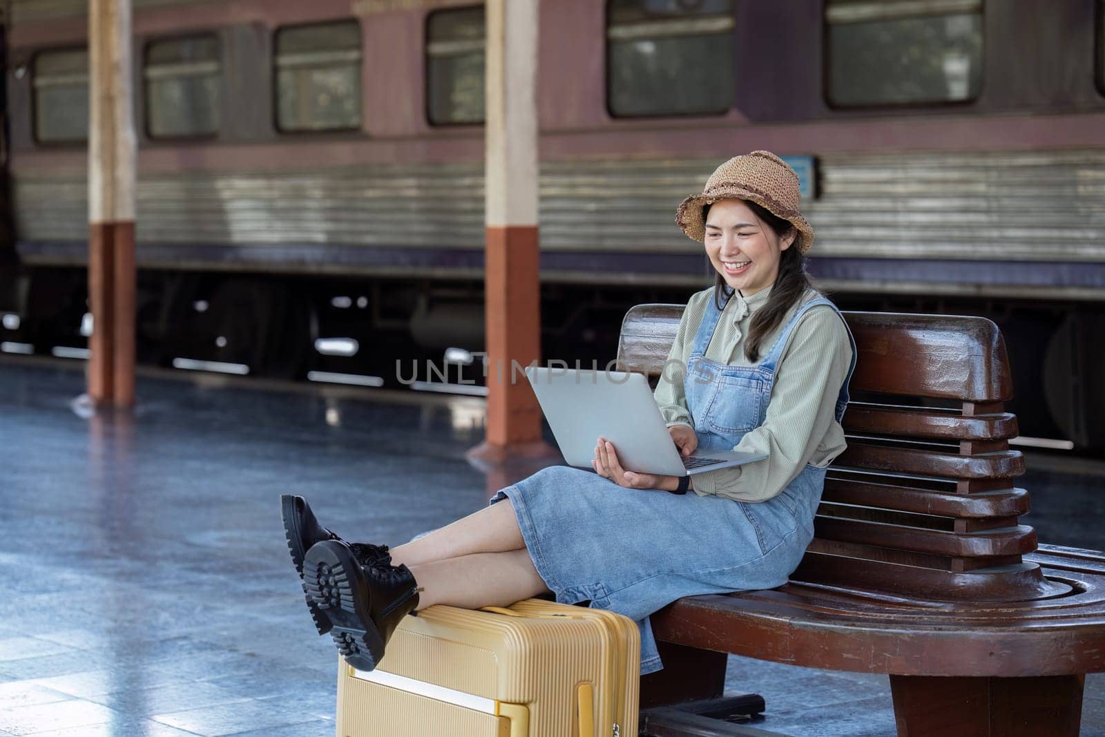 Woman traveler with backpack using laptop to planning vacation on holiday relaxation at the train station.