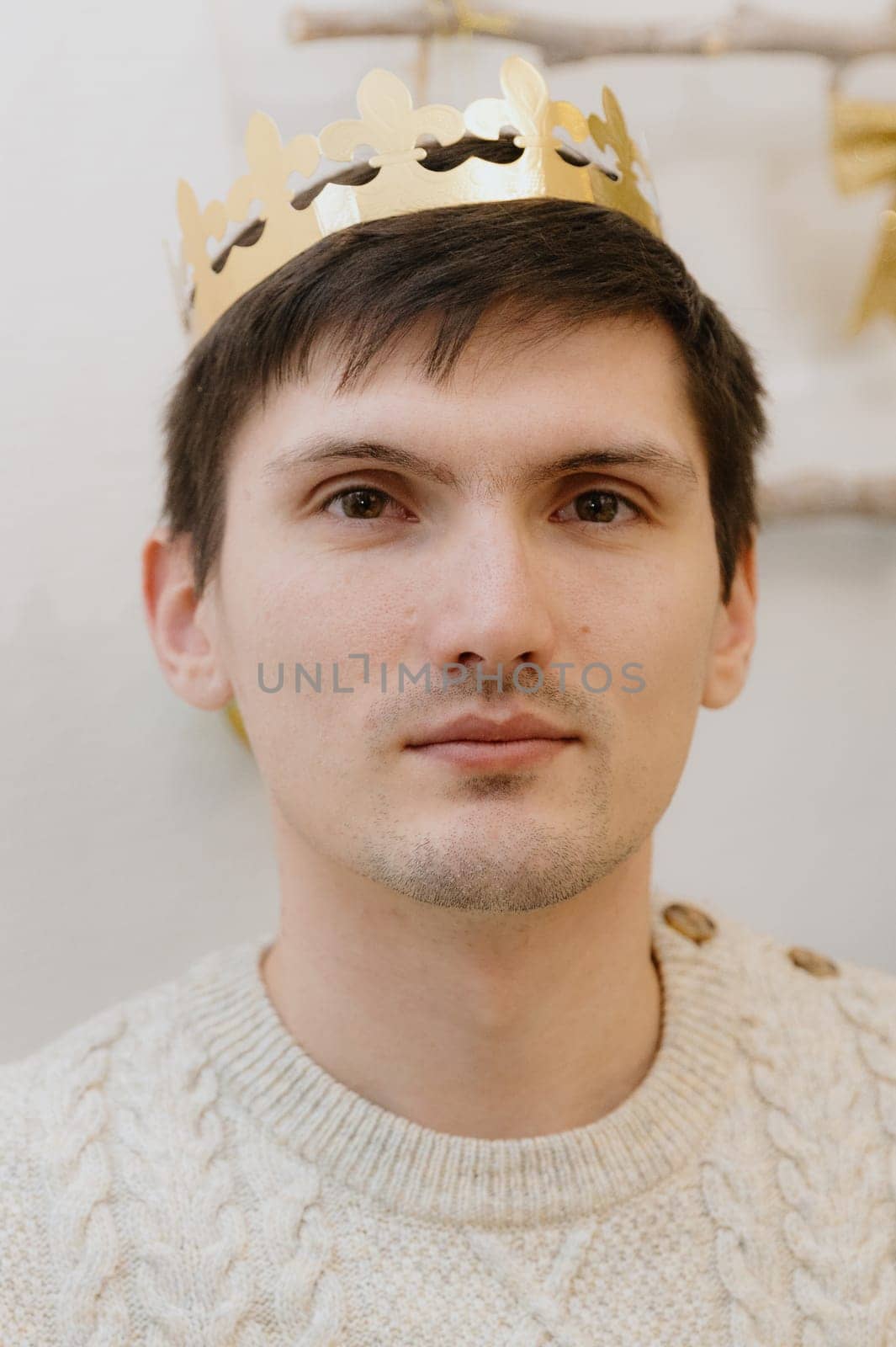 Portrait of one young handsome Caucasian man with a golden paper crown on his head, after eating a royal galette and finding a gift, close-up side view.