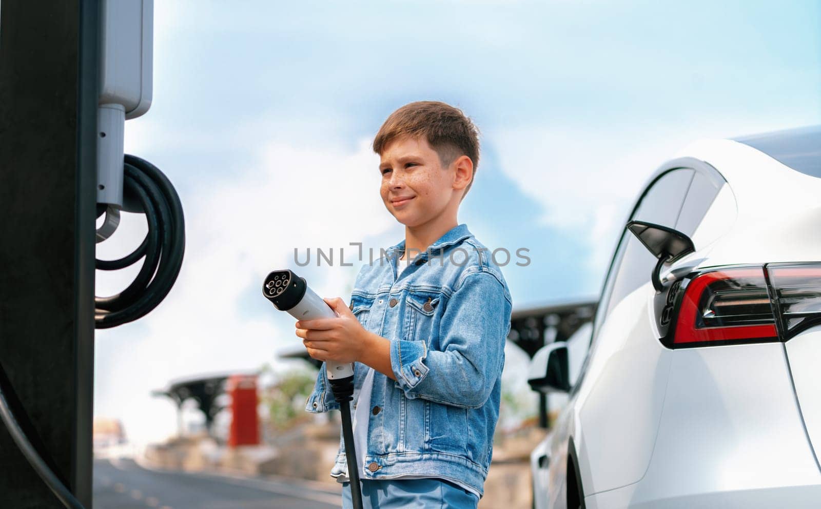 Little boy recharging eco-friendly electric car from EV charging station. EV car road trip travel concept for alternative transportation powered by clean renewable and sustainable energy. Perpetual