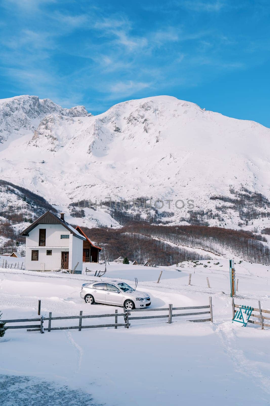 Snow-covered silvery car stands near the fence of a cottage in a village in a mountain valley. High quality photo