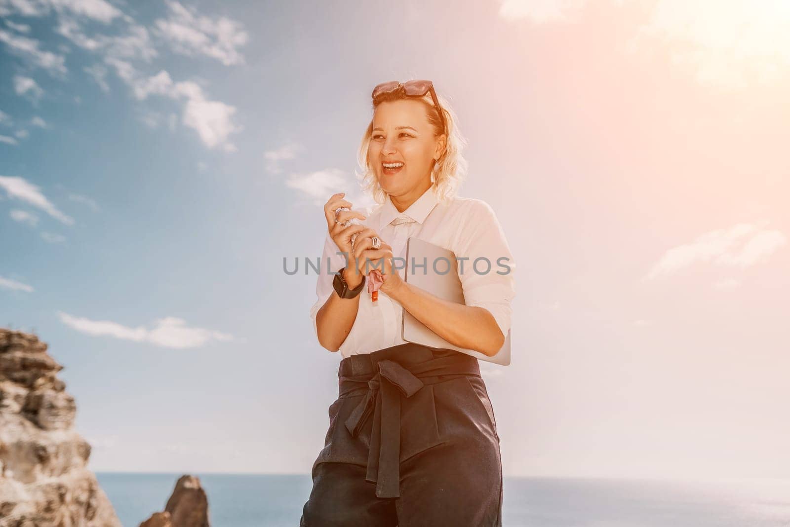 Digital nomad, Business woman working on laptop by the sea. Pretty lady typing on computer by the sea at sunset, makes a business transaction online from a distance. Freelance, remote work on vacation