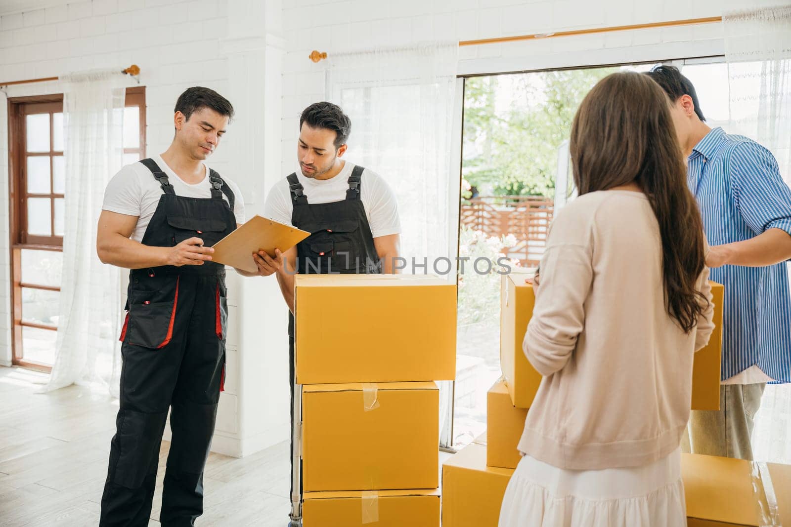 Couple checks moving checklist worker holds cardboard box. Professional movers ensure smooth relocation service. Teamwork and efficient home moving displayed. Movind Day