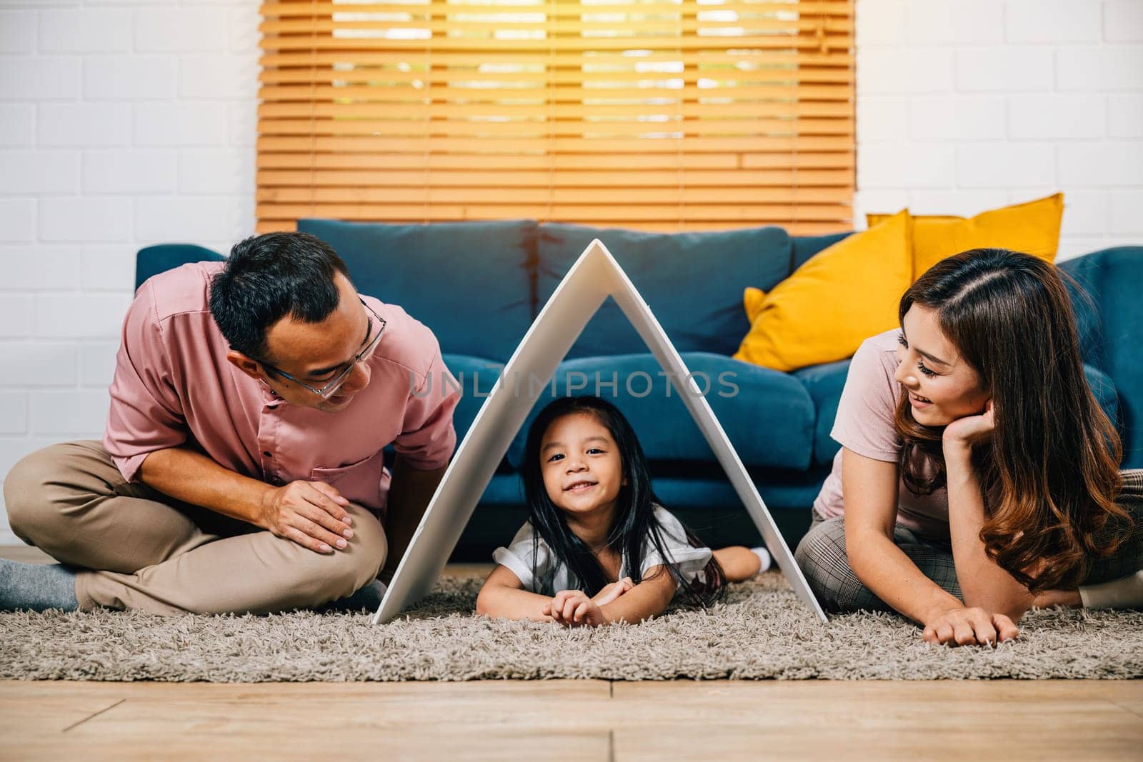 A portrait of a harmonious family sitting on a couch holding a cardboard roof by Sorapop