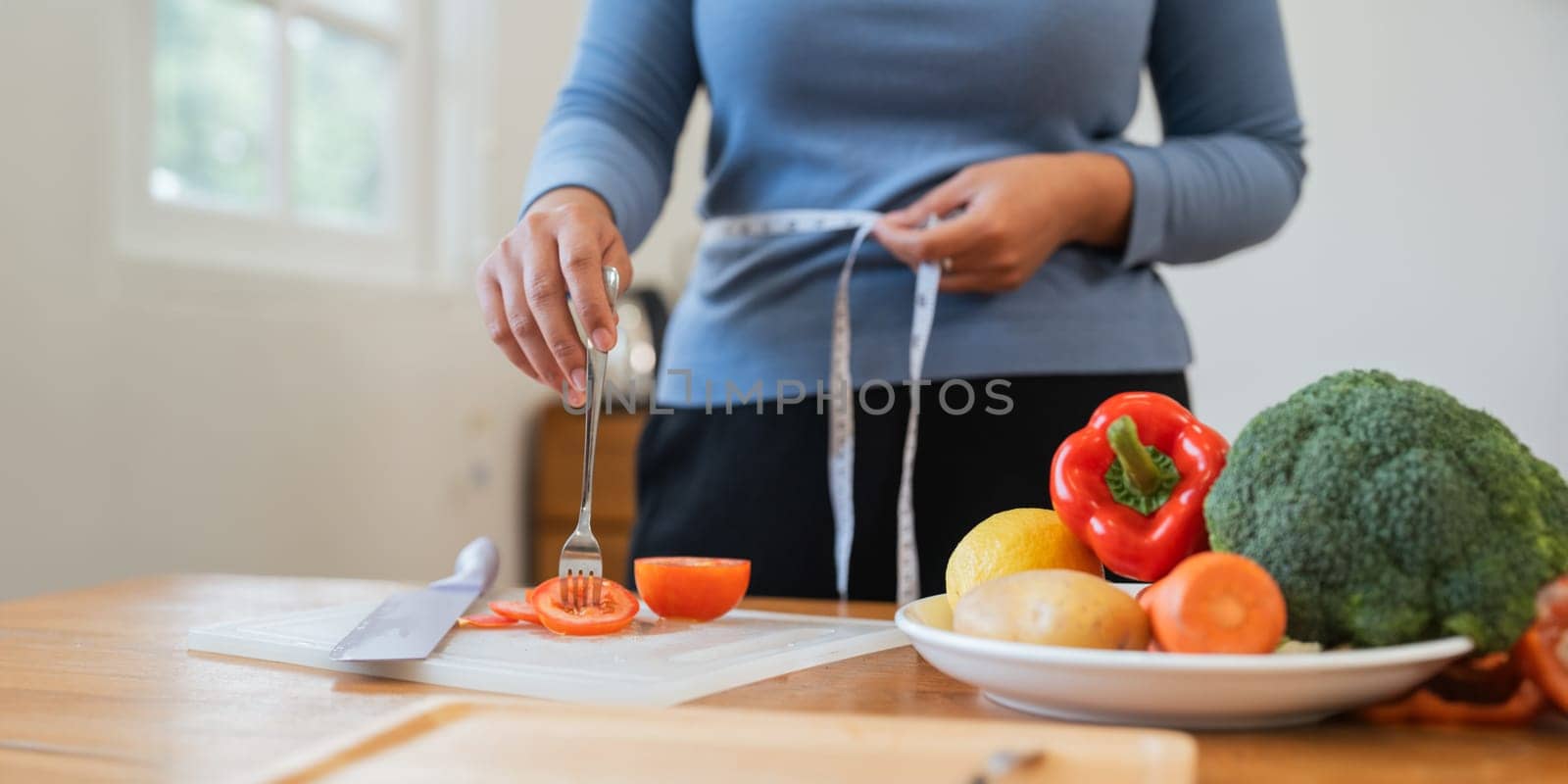 Young woman asian measure her waist in the kitchen the with vegetables and fruits. Concept of healthy eating and dieting by nateemee