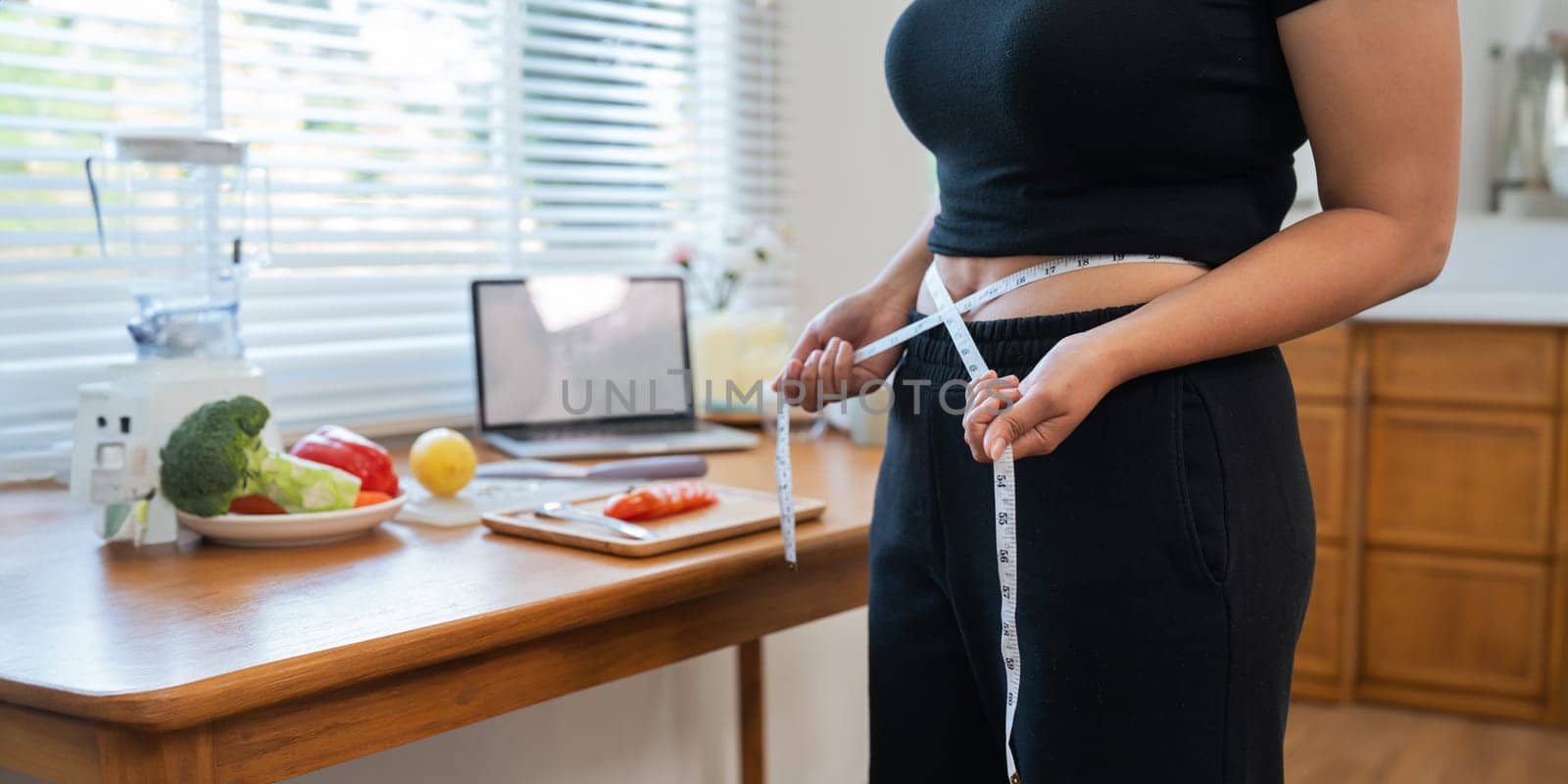 Young woman asian measure her waist in the kitchen the with vegetables and fruits. Concept of healthy eating and dieting.