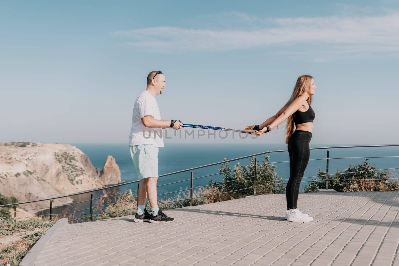 Happy Middle aged couple or friends practicing nordic walking in park near sea. Mature couple with trekking poles walking, practicing Nordic walking outdoors. Aging youthfully and sport concept.