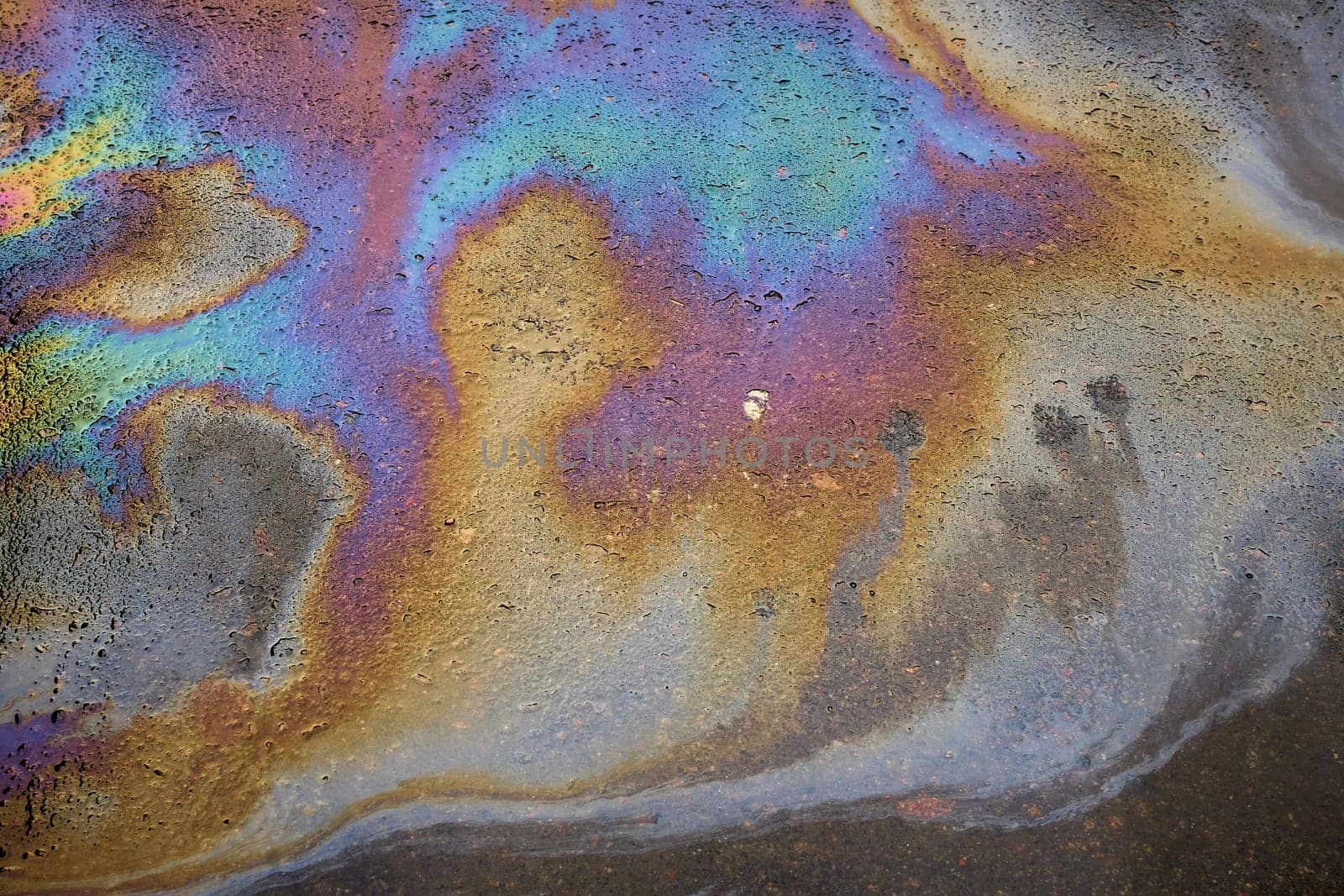 Multi-colored toxic stains of spilled gasoline on wet asphalt during the rain. Rain washed away car oil or fuel flowing from a faulty car in a parking lot.